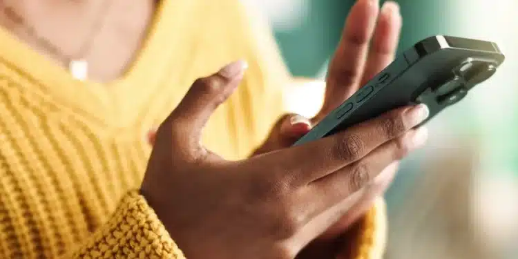 Pessoa digitando em um smartphone, com mãos visíveis, usando um suéter amarelo.