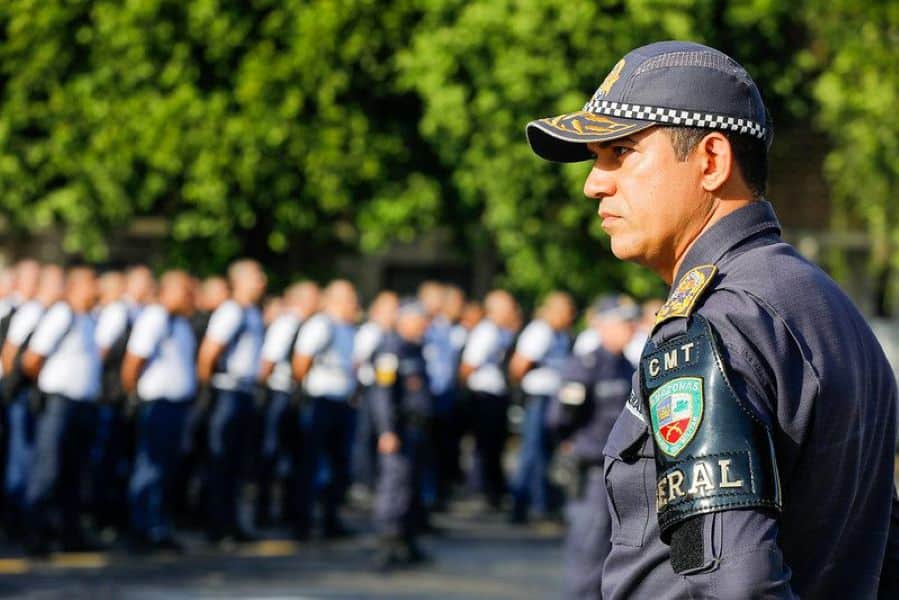 Policial de segurança pública do Amazonas em uniforme, com outros agentes ao fundo, durante um evento de promoção e reajuste salarial.