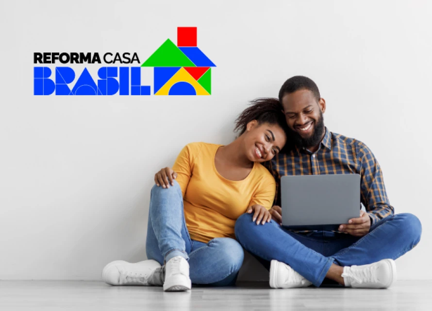 Casal brasileiro sorrindo usando notebook para planejar reforma da casa, representando as opções disponibilizadas pelo Programa Reforma Casa Brasil