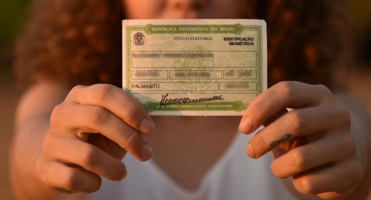 Pessoa segurando o título de eleitor brasileiro, documento oficial de identificação eleitoral.