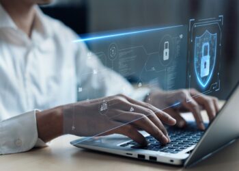Profissional utilizando notebook com interface digital de proteção de dados, representando práticas de cibersegurança.