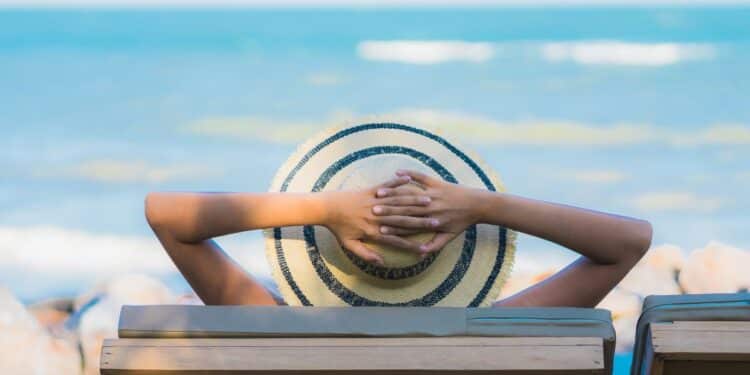 Pessoa relaxando em cadeira de praia com chapéu, olhando o mar durante período de descanso.