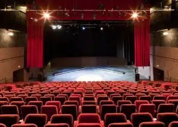 Palco de um teatro, com cadeiras vermelhas e luzes direcionadas ao palco, representando os caminhos profissionais no universo teatral.