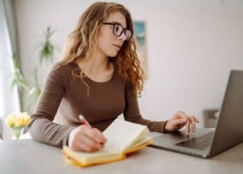Estudante utilizando notebook e fazendo anotações durante estudo online para provas como Enem e vestibulares.