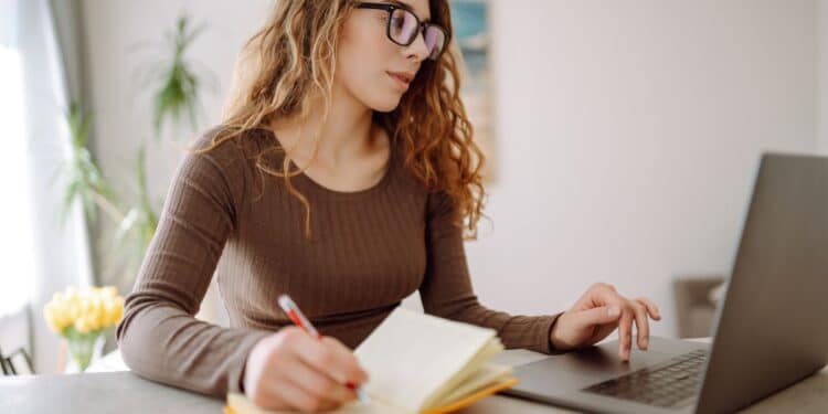 Estudante utilizando notebook e fazendo anotações durante estudo online para provas como Enem e vestibulares.