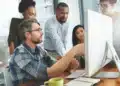 Equipe discutindo em escritório moderno, focados em tarefa na tela do computador.