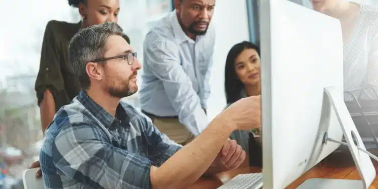 Equipe discutindo em escritório moderno, focados em tarefa na tela do computador.