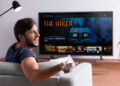 Homem sorridente sentado no sofá assistindo filme em smart TV de tela grande na sala de estar