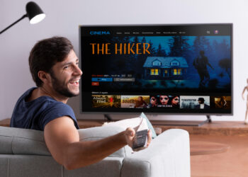 Homem sorridente sentado no sofá assistindo filme em smart TV de tela grande na sala de estar