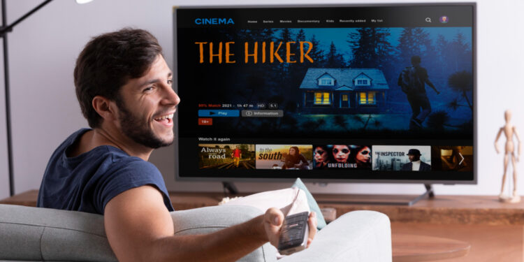 Homem sorridente sentado no sofá assistindo filme em smart TV de tela grande na sala de estar