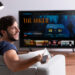 Homem sorridente sentado no sofá assistindo filme em smart TV de tela grande na sala de estar