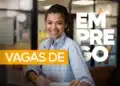 Mulher jovem de camisa azul clara sorrindo em escritório com texto "Vagas de Emprego" sobreposto