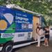 Van itinerante azul do SINE Casa do Trabalhador estacionada em área arborizada com duas mulheres no atendimento