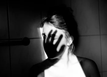 Mulher em preto e branco com sombra de mão no rosto simbolizando violência e proteção contra agressões.