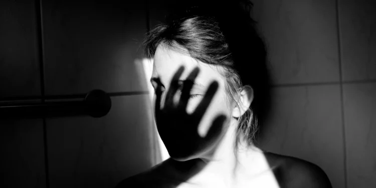 Mulher em preto e branco com sombra de mão no rosto simbolizando violência e proteção contra agressões.