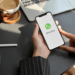 Mãos segurando smartphone com tela de abertura do WhatsApp sobre mesa