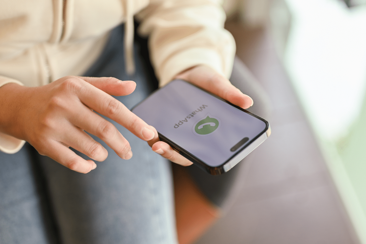 Pessoa com moletom bege segura smartphone exibindo logotipo verde do WhatsApp na tela roxa de carregamento