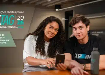 Banner oficial do XTAG 2026, programa de estágio da XP Inc., com dois jovens participantes olhando para a tela do celular em ambiente corporativo
