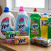 Produtos Ypê incluindo detergente, amaciante, multiuso, sabão em barra e lã de aço dispostos em bancada de madeira.