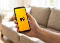 Mão masculina segurando celular com app 99 aberto na tela.
