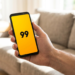 Mão masculina segurando celular com app 99 aberto na tela.