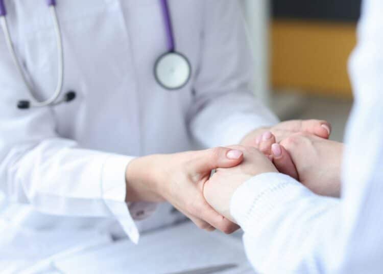 Médica segura mãos de paciente em gesto de acolhimento.