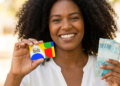 Mulher negra segurando cartão do Bolsa Família e cédulas de R$ 100,00.
