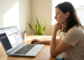 Mulher concentrada usando laptop com abas abertas do ChatGPT, Google Gemini e Microsoft Copilot em mesa de madeira.