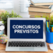 Notebook sobre mesa de madeira exibindo "CONCURSOS PREVISTOS" em tela azul, cercado por livros, câmera e plantas.