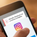 Mão segurando smartphone com notificação do Instagram sobre mudanças nas conversas protegidas e logo do app.