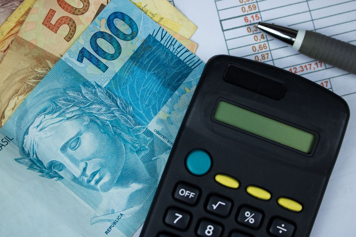 Notas de real brasileiro ao lado de calculadora sobre planilha.