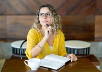 Mulher pensativa com caderno aberto em café aconchegante.