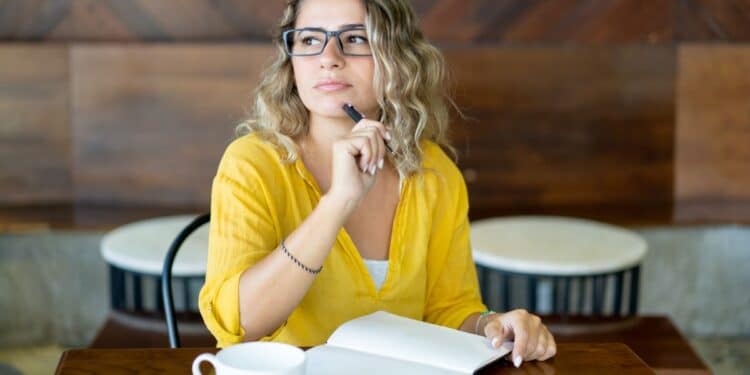 Mulher pensativa com caderno aberto em café aconchegante.