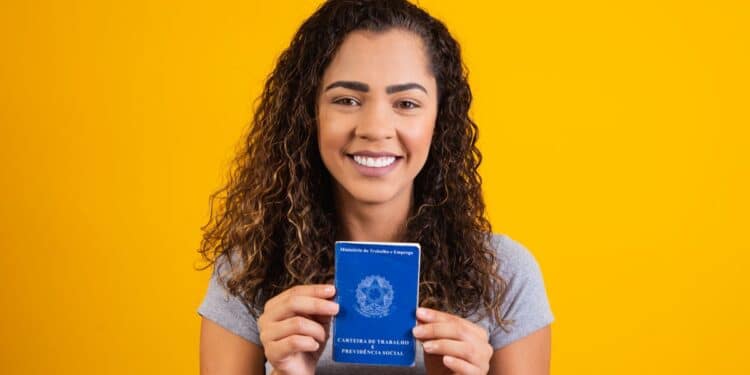 Jovem sorridente exibe Carteira de Trabalho brasileira em fundo amarelo.
