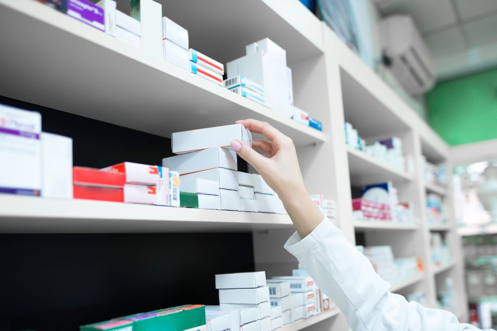 Mão feminina colocando uma caixa de medicamentos em uma prateleira da farmácia.