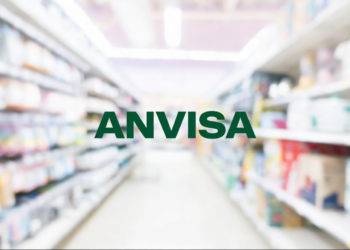 Nome "ANVISA" em corredor de farmácia com prateleiras de medicamentos.