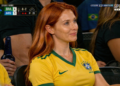 Mulher sorrindo sentada em arquibancada de jogo de futebol.