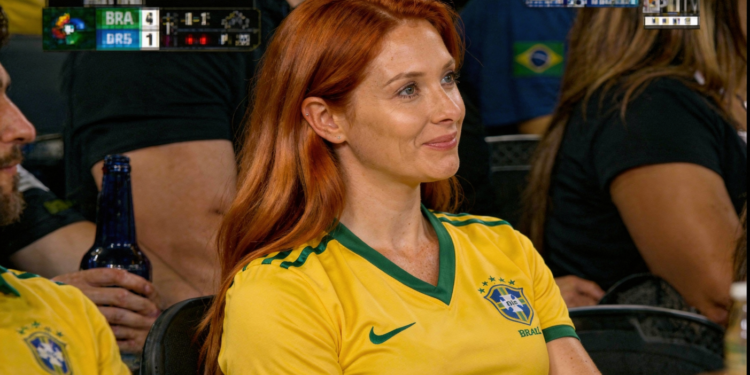 Mulher sorrindo sentada em arquibancada de jogo de futebol.