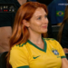 Mulher sorrindo sentada em arquibancada de jogo de futebol.