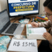 Jovem de óculos estuda apostila em mesa com notebook, monitor exibindo "Concurso de Prefeitura", dinheiro e caderno com "R$ 13 MIL"
