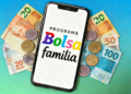 Programa Bolsa Família exibido em smartphone com cédulas de brasileiras no fundo.