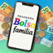 Programa Bolsa Família exibido em smartphone com cédulas de brasileiras no fundo.