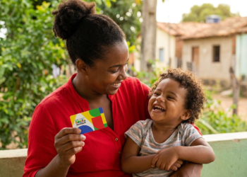 Mãe segura cartão Bolsa Família ao lado do filho.