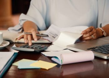 Mulher organiza finanças com calculadora e documentos.