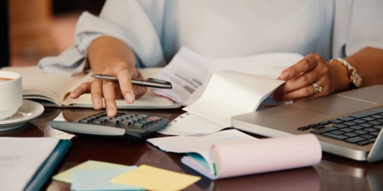 Mulher organiza finanças com calculadora e documentos.