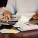 Mulher organiza finanças com calculadora e documentos.
