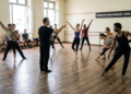 Bailarinos ensaiam em sala com piso de madeira, diretor central aponta, faixa "Companhia de Dança Brasileira - Ensaio Aberto".