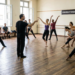 Bailarinos ensaiam em sala com piso de madeira, diretor central aponta, faixa "Companhia de Dança Brasileira - Ensaio Aberto".