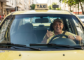 Taxista sorridente em táxi amarelo nas ruas.