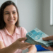 Mulher jovem de camisa rosa sorri ao receber maço de notas de R$ 100 de outra pessoa em ambiente de escritório.